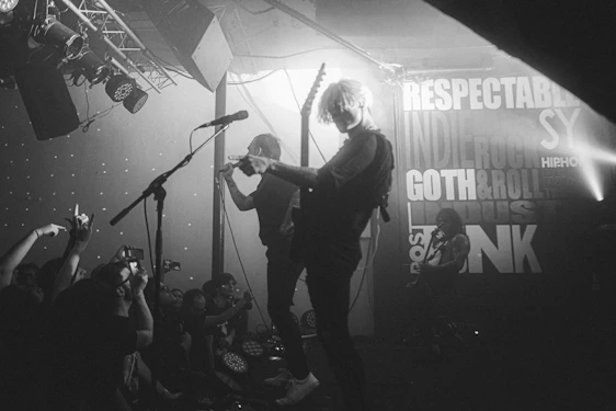 Black-and-white photo of Headrush performing live, with bright red stage lights cutting through the darkness.