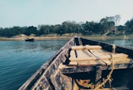 Traditional wooden boat floating on clear river water surrounded by green foliage.