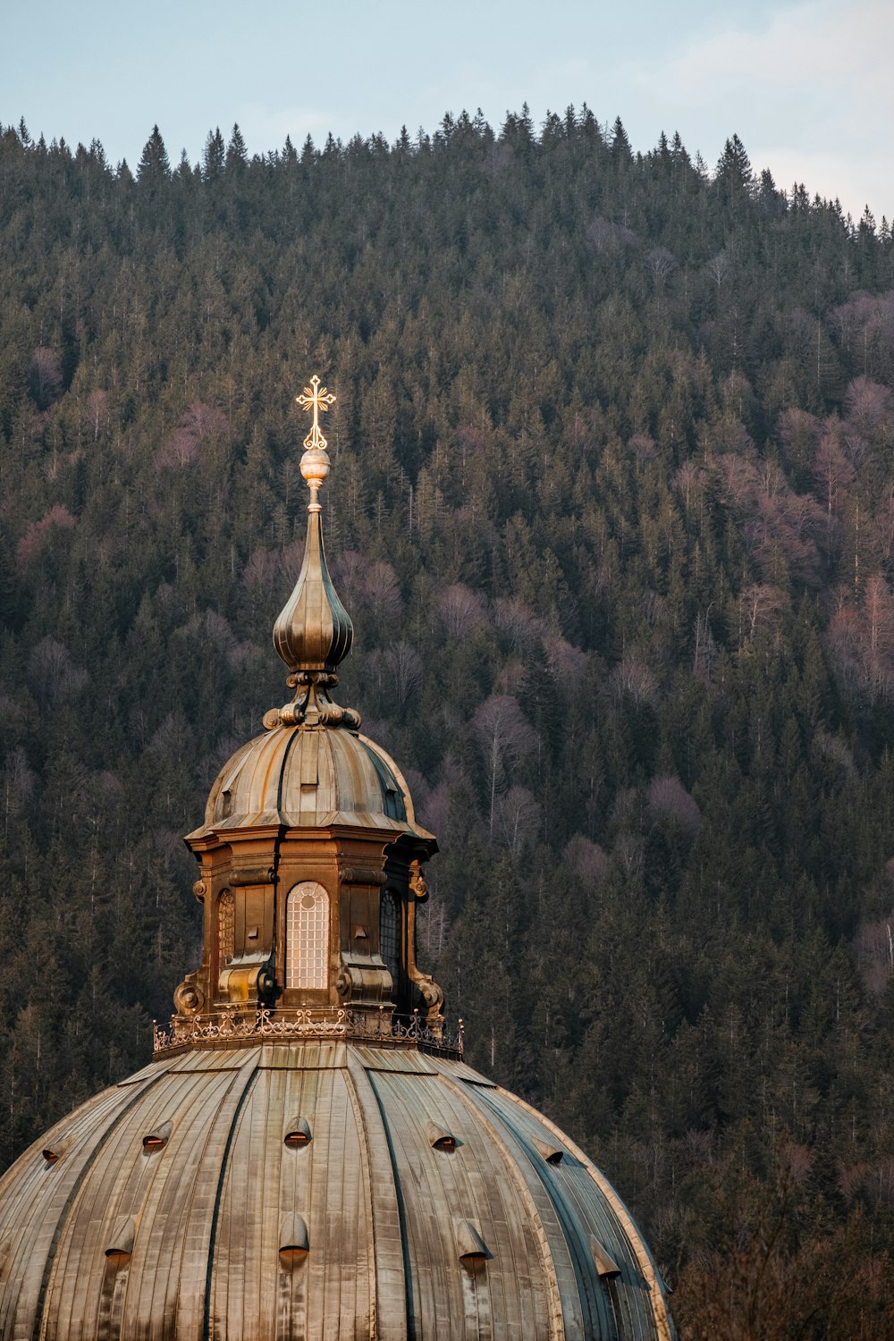 a gold domed building with a gold cross on top of a hill with trees and a hill in