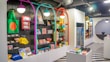 A brightly lit retail store interior featuring colorful and neatly organized merchandise displays. The walls have arches with vibrant colors like purple, teal, red, and yellow. Shelves contain a variety of items including bags, books, and small accessories. The flooring has a striped black and white pattern, and modern pendant lights hang from the ceiling.