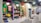 A brightly lit retail store interior featuring colorful and neatly organized merchandise displays. The walls have arches with vibrant colors like purple, teal, red, and yellow. Shelves contain a variety of items including bags, books, and small accessories. The flooring has a striped black and white pattern, and modern pendant lights hang from the ceiling.