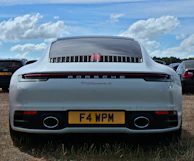 A pristine white Porsche 911 Carrera parked in front of a modern luxury villa at sunset.