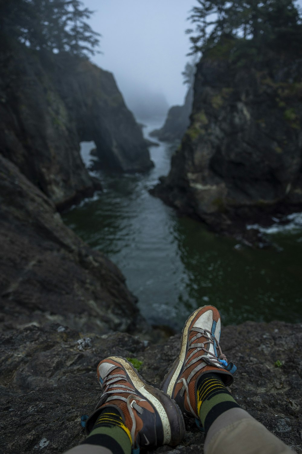 a person's feet on a rock ledge above a river