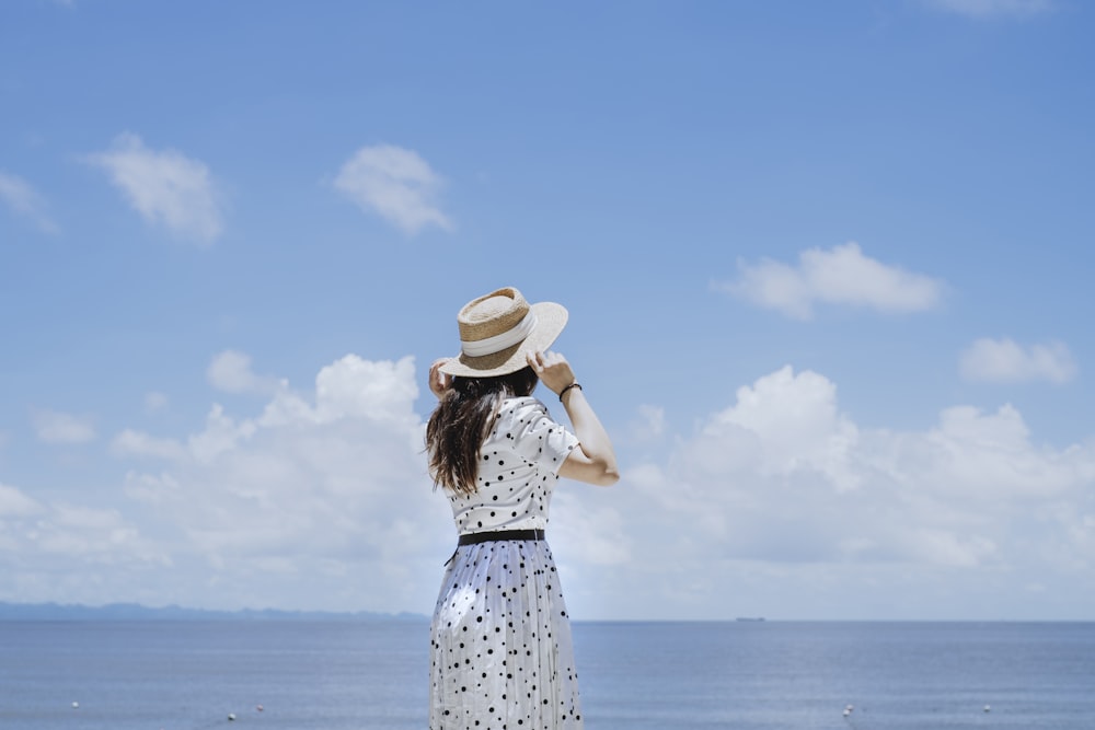 a person in a dress and hat standing in front of a body of water