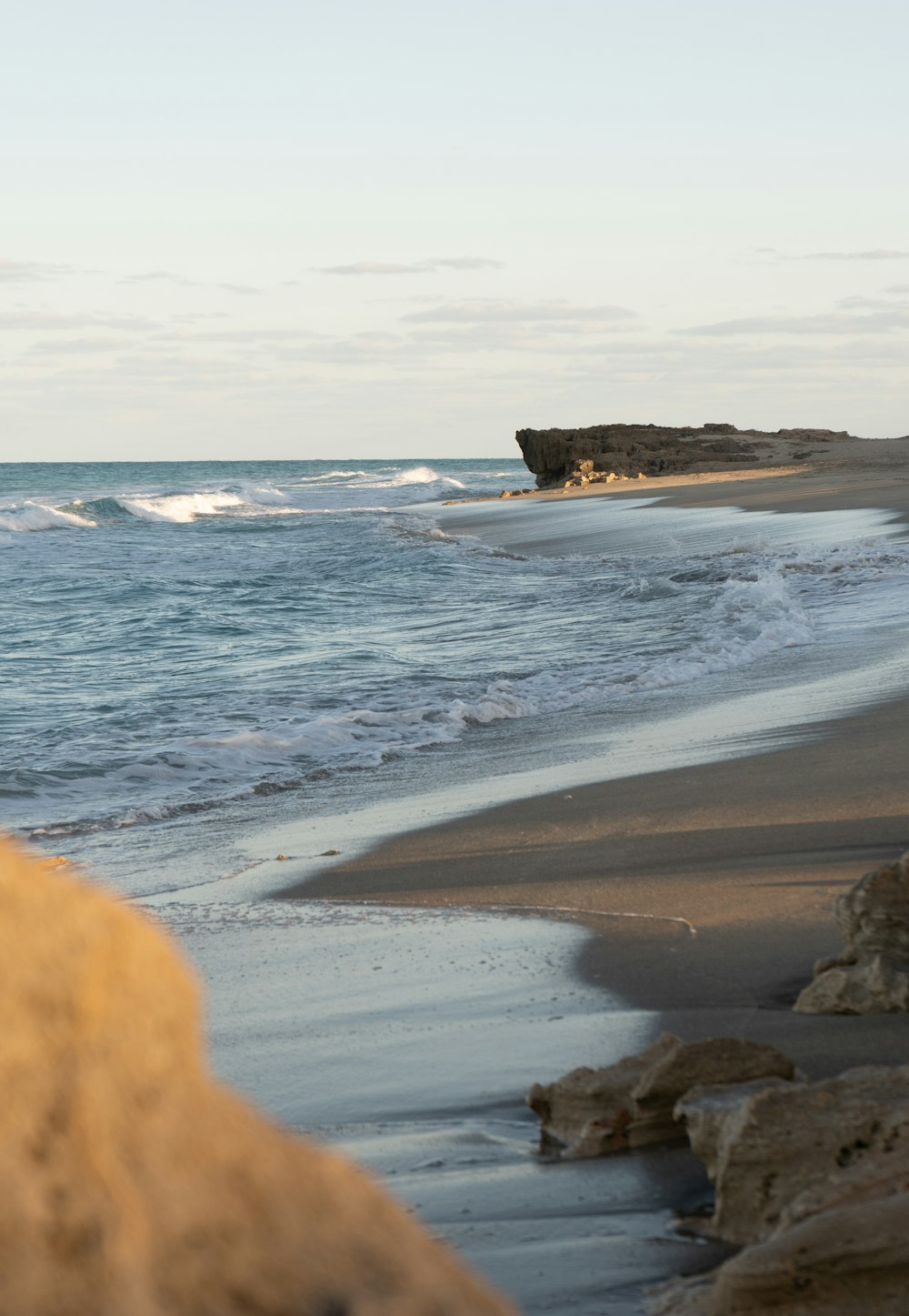 una mano sosteniendo un pulgar hacia arriba en una playa con olas rompiendo sobre ella