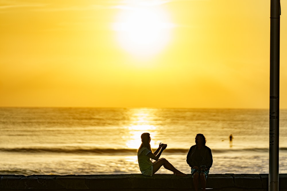 a man and a woman sitting on a beach looking at the sunset