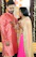 A joyful couple dressed in traditional Indian attire smiling warmly against a backdrop of maroon and gold decorations.