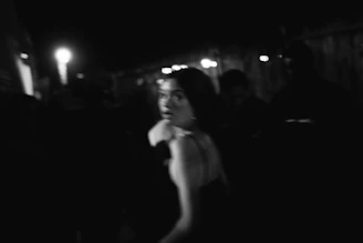 Black-and-white photo of a woman glancing back in a dark, blurred crowd