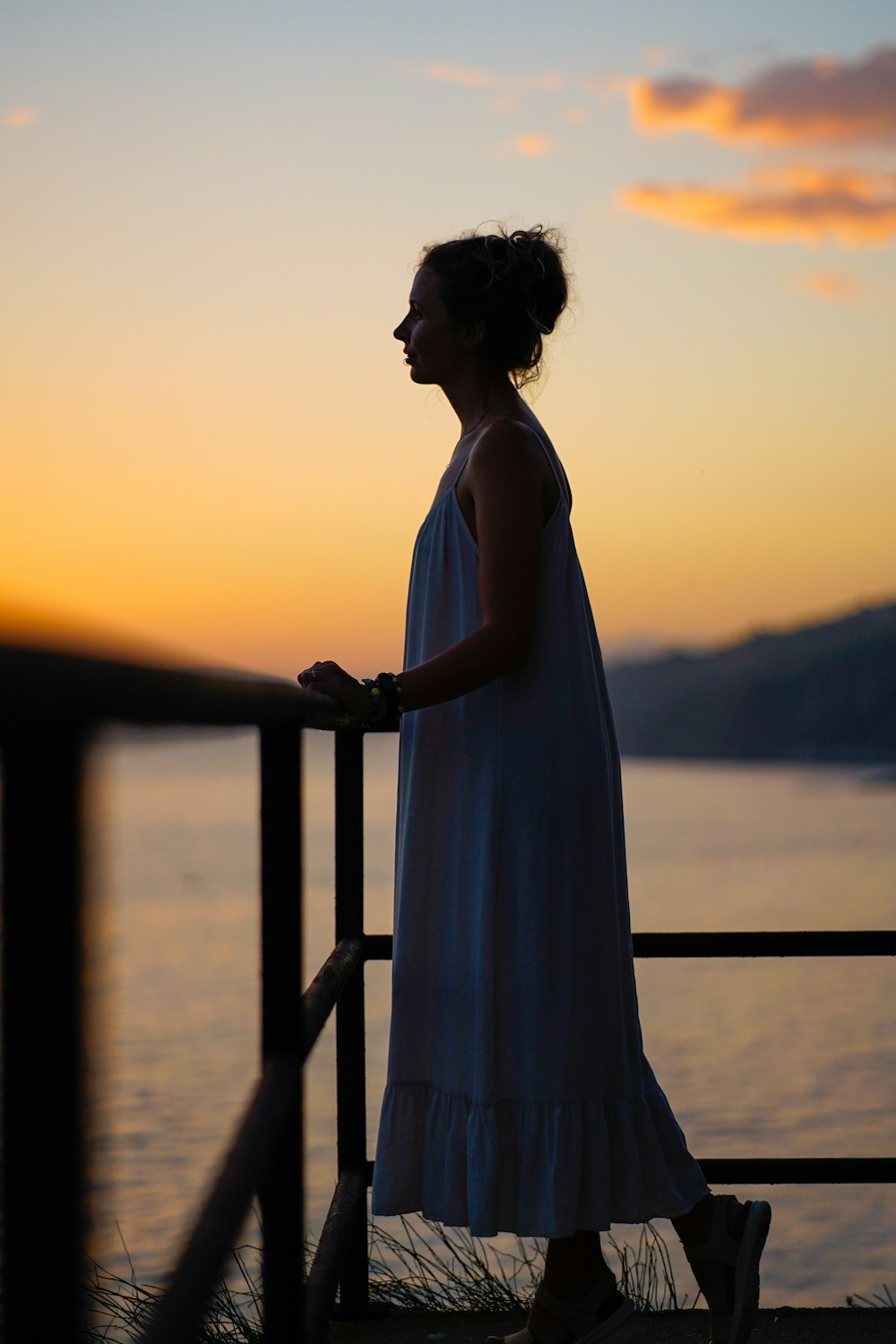 a person in a dress standing on a balcony overlooking the water