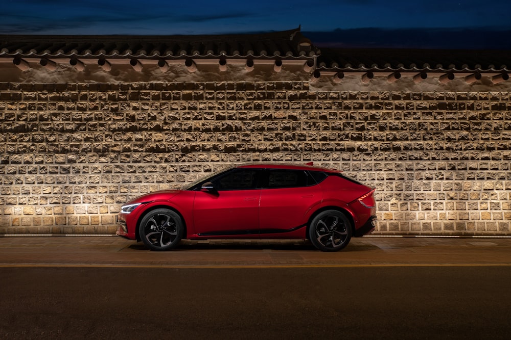 a red car parked in front of a stone wall