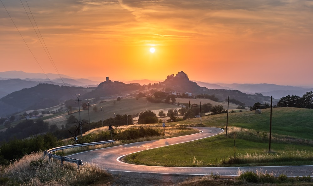 a road with grass and trees on the side with a sunset in the background