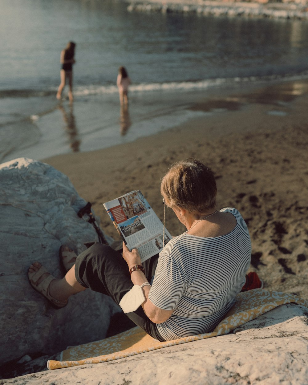 une personne assise sur un rocher lisant un livre sur une plage