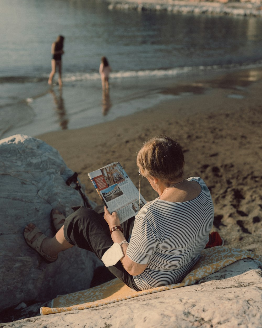 해변에서 책을 읽고 있는 바위에 앉아 있는 사람