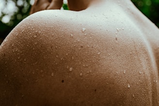 Close-up of water droplets glistening on sun-kissed skin, emphasizing texture and light in a swimwear editorial.