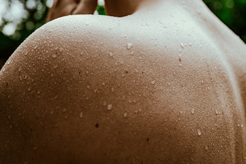Close-up of water droplets glistening on sun-kissed skin, emphasizing texture and light in a swimwear editorial.