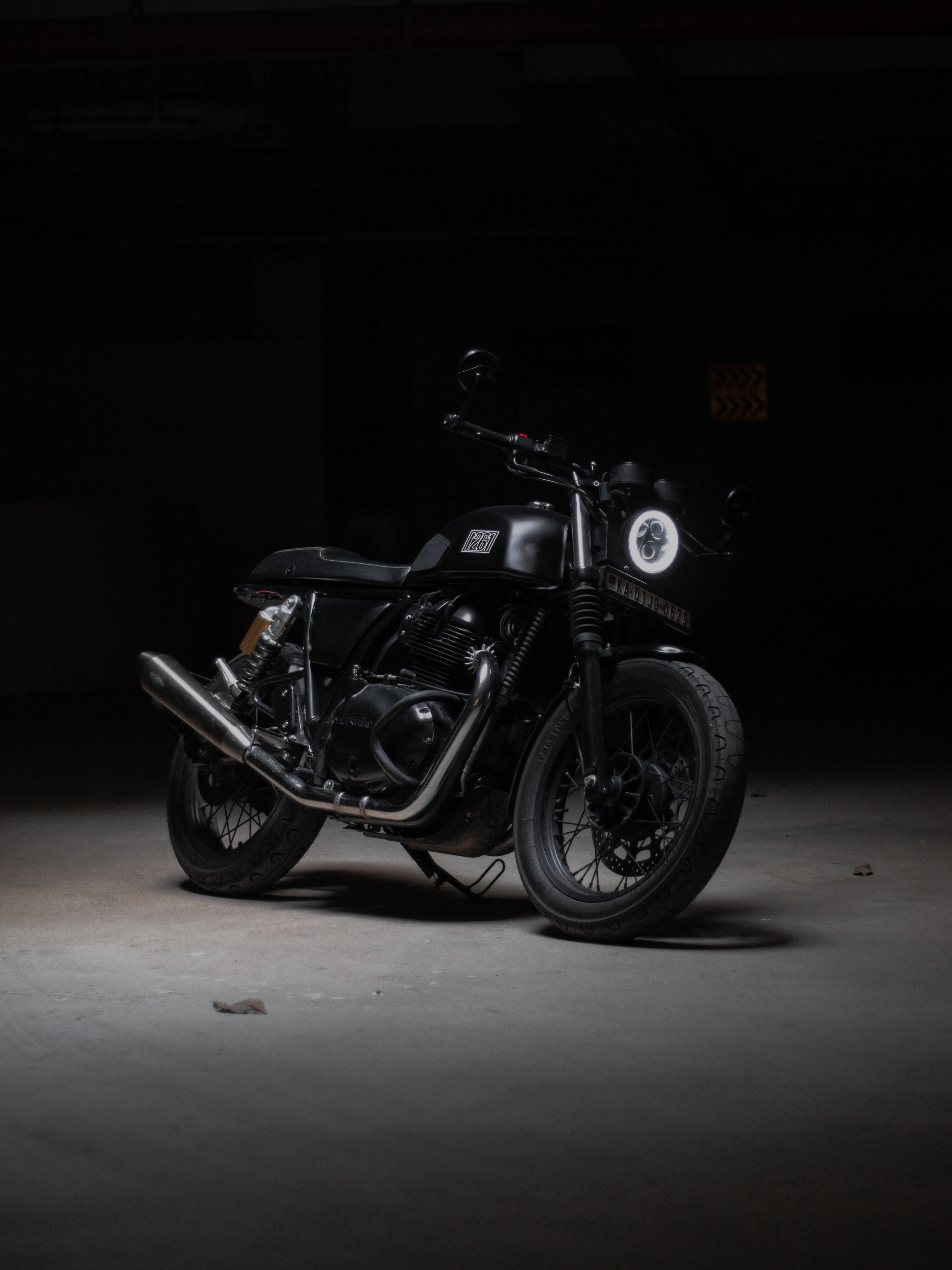 A black twin-cylinder motorcycle under a single spotlight in a dark garage