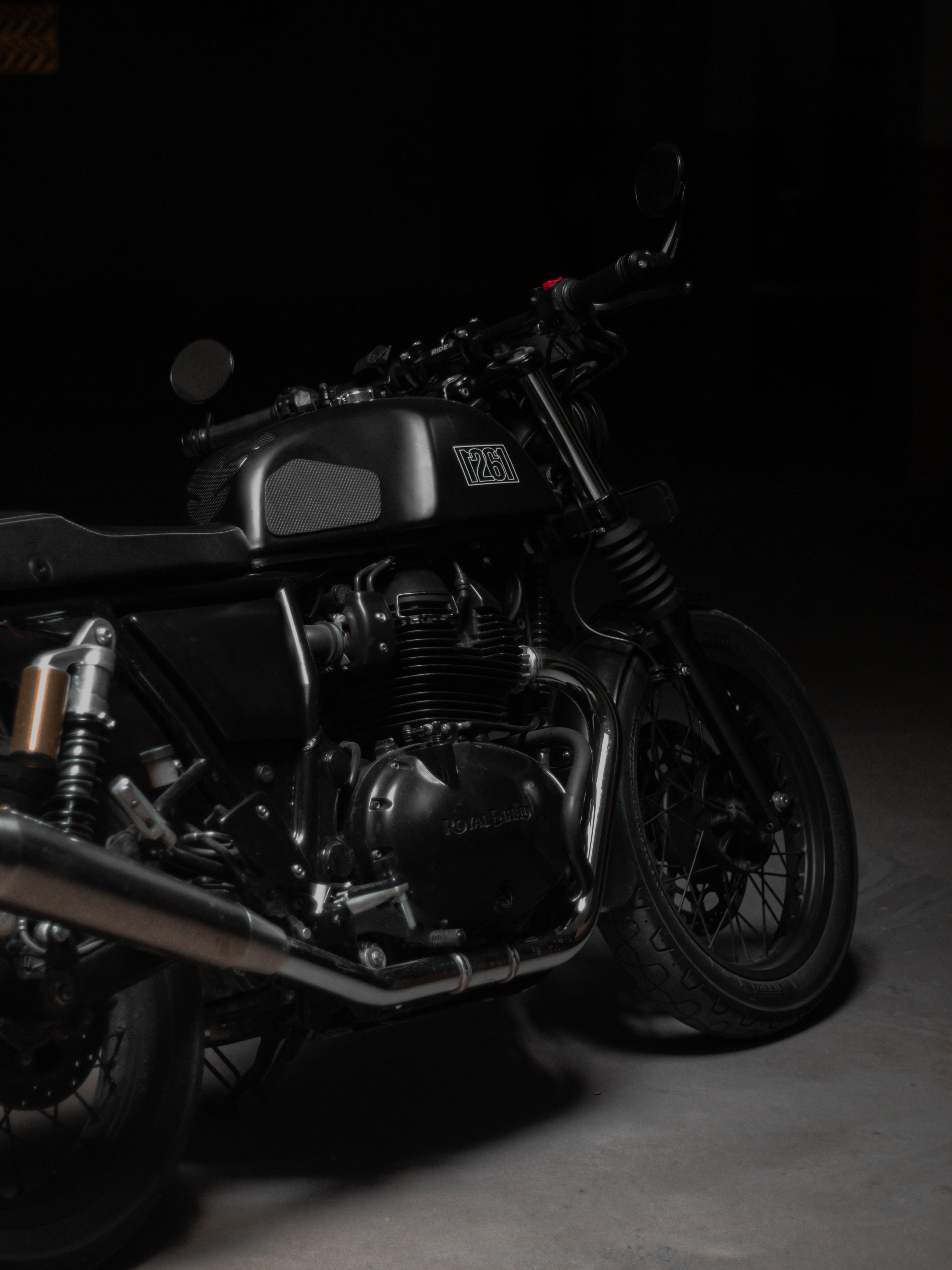 Close-up of a black motorcycle's twin-cylinder engine, exhaust and fuel tank in low light