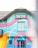 A building with vibrant, colorful street art features a prominent sign with the word 'SEDE'. The facade is painted in bright blue, pink, and orange with abstract, flowing patterns. There are windows and string lights hanging across the front.