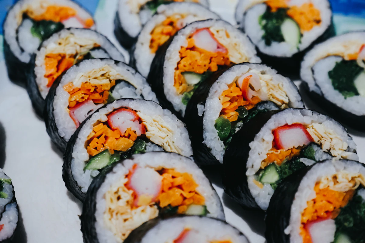 Fila ravvicinata di rotoli di kimbap tagliati, con surimi, carota, cetriolo e uovo ben visibili