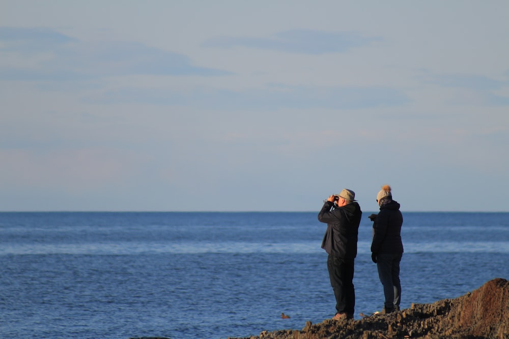 a group of people standing on a rocky shore looking at the ocean