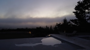 Wide shot of a serene poolside scene at dusk, with a model in sleek swimwear reflecting the luxury minimalism gap index celebrates.