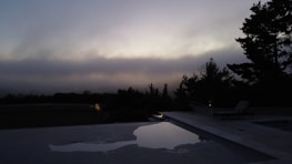 A serene backyard pool at dusk, lights glowing softly in the water.