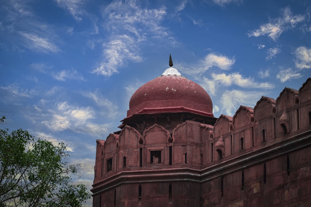 a large brick building with a red dome and a tree in front