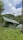 Several green tents are set up in a grassy field, surrounded by lush greenery and hills. The sky is partially cloudy, creating a serene and peaceful outdoor camping scene.