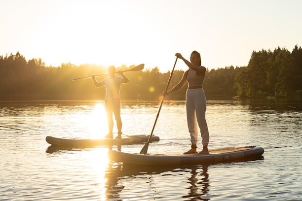Two people paddling side by side on a sleek electric stand-up paddleboard catamaran at sunset.