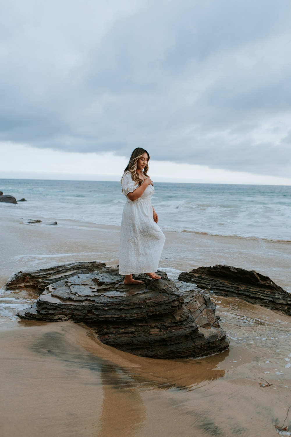 a person in a white dress standing on a rock by the water