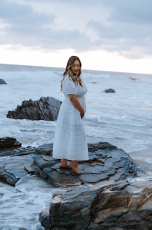 a person in a white dress standing on a rocky beach