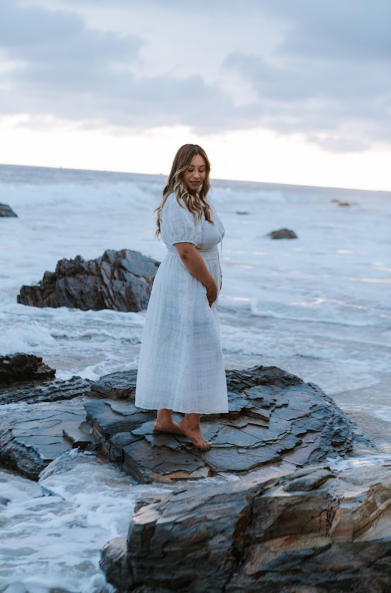 a person in a white dress standing on a rocky beach