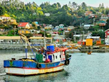 A colorful fishing boat docked near a small island village with wooden huts.