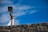 A surveillance camera mounted on a metal pole is positioned above a stone wall, with a clear blue sky in the background.