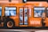 A brightly colored bus with promotional graphics parked at night under artificial lighting. The bus features large images of smiling people and text promoting a radio station with the slogan 'LISTEN & WIN'. The interior is partially visible through the windows.