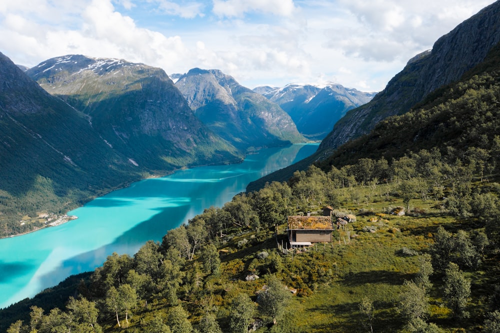 Una casa en una colina junto a un lago rodeado de montañas