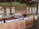 A spacious store interior with shelves stocked with various tea products. The shelves are made of wood and hold boxes and tins of tea neatly arranged. The logo 'Haple Tea' is displayed on the brick wall. The foreground features wooden tables with additional tea products, including tins with red lids and brown paper bags.