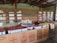 A spacious store interior with shelves stocked with various tea products. The shelves are made of wood and hold boxes and tins of tea neatly arranged. The logo 'Haple Tea' is displayed on the brick wall. The foreground features wooden tables with additional tea products, including tins with red lids and brown paper bags.