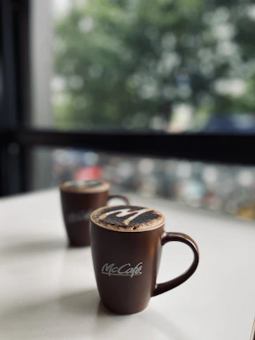 A cozy scene showing 12oz and 16oz coffee cups with personalized logos steaming beside a notebook.