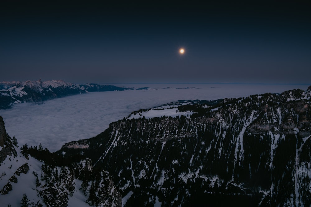 Una montagna innevata con la luna nel cielo