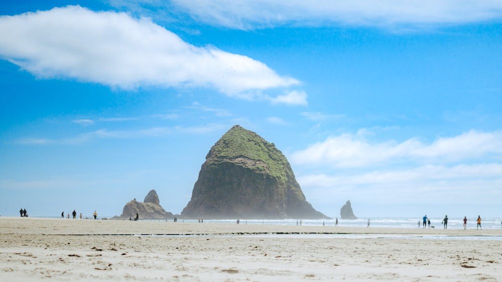 a group of people walking on a beach with large rocks in the background