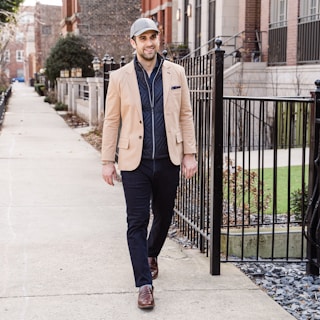 A man confidently walking down a city street wearing a trendy jacket and slim-fit jeans.