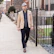 A man in a sleek turncoat smiling while walking through a city park.
