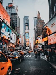A vibrant city street lined with shops and office buildings, busy with people and cars.