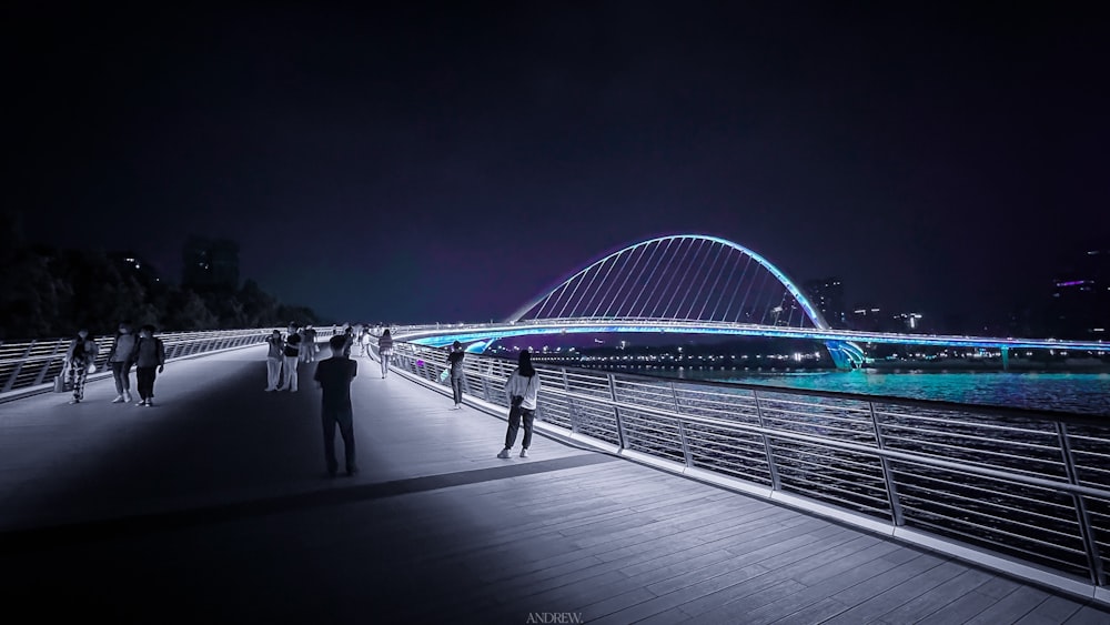 a group of people walking on a bridge over water at night