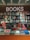 A bookstore interior features a glowing 'BOOKS' sign with circular lights. Below, shelves are filled with various genres, including graphic design, music, and interior design. The display table in front showcases an assortment of colorful books and magazines, including works on art, fashion, and architecture.