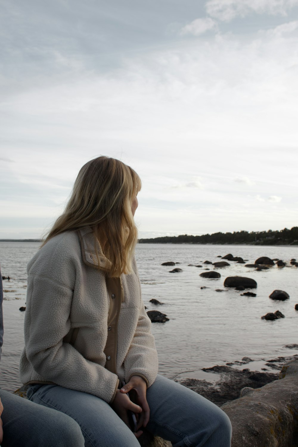 a woman sitting on a rock looking at the water