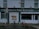 A storefront of a pork butcher shop with the name 'F. Heterich's Pork Butchers' prominently displayed. The facade includes an image of a pig with the words 'Pork Butcher' beneath it. Two bicycles are parked in front of the shop. A 'No Parking' sign is present, allowing loading for 30 minutes. The shop windows display additional text indicating sausage manufacturing.