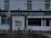A storefront of a pork butcher shop with the name 'F. Heterich's Pork Butchers' prominently displayed. The facade includes an image of a pig with the words 'Pork Butcher' beneath it. Two bicycles are parked in front of the shop. A 'No Parking' sign is present, allowing loading for 30 minutes. The shop windows display additional text indicating sausage manufacturing.
