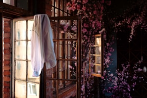 A soft pastel pink blouse with puff sleeves hanging near a window with greenery outside